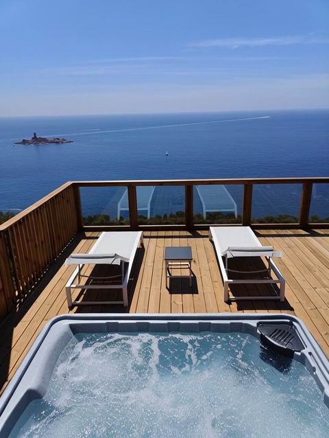 Spa extérieur sur une terrasse en bois face à la mer avec deux bains de soleil