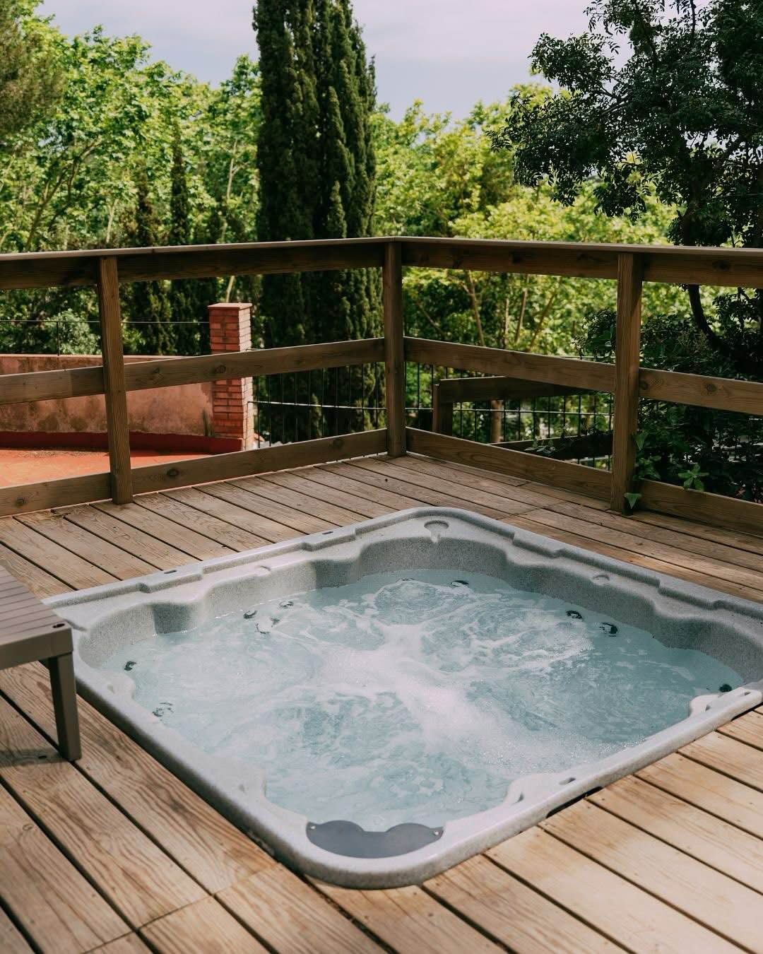 Spa clair encastré dans une terrasse en bois au milieu d'un jardin arboré