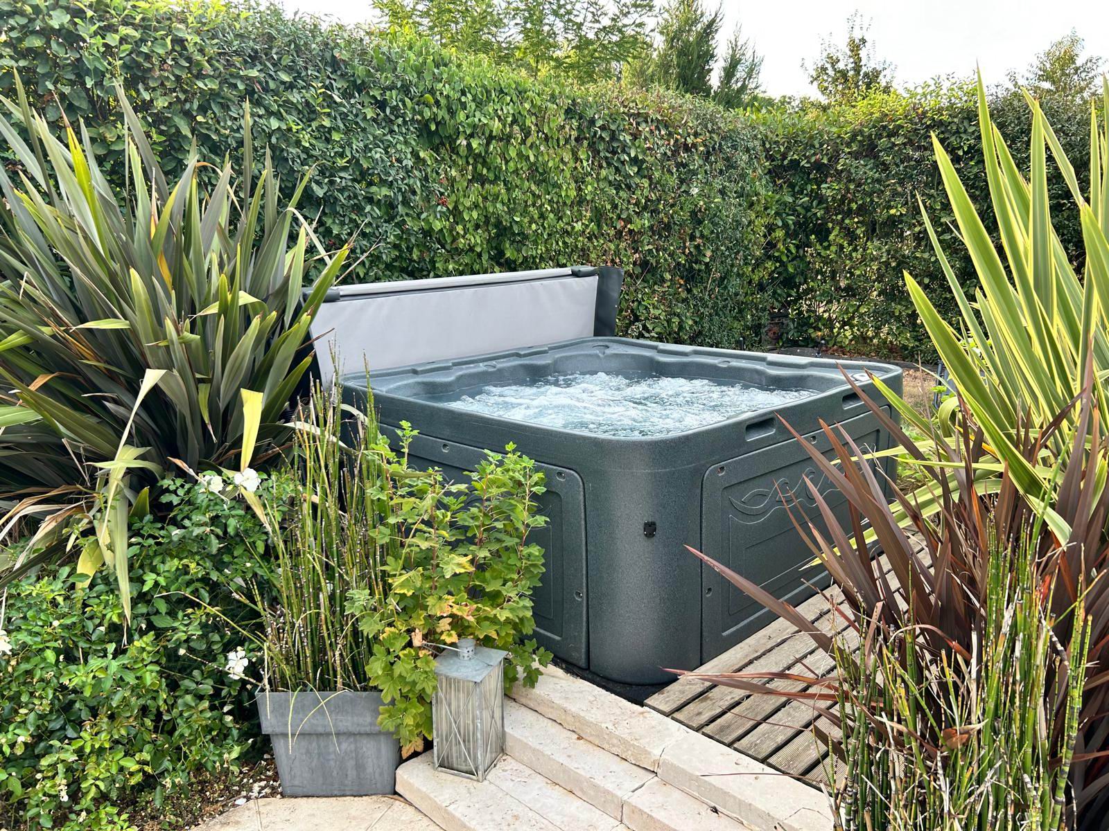 Spa anthracite en fonctionnement dans un jardin avec sa couverture relevée