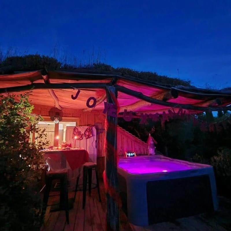 Spa extérieur éclairé en violet sur une terrasse couverte à la tombée de la nuit