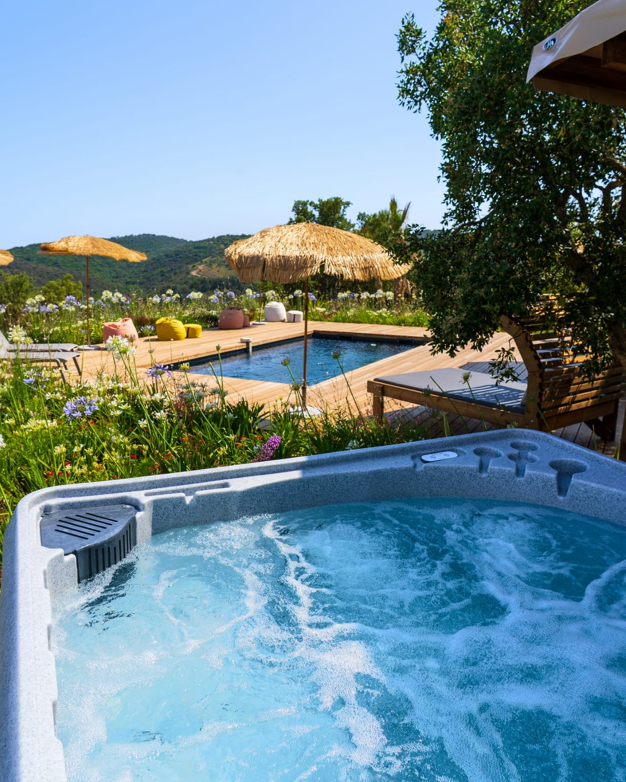 Spa en fonctionnement au premier plan d'une terrasse avec piscine et parasols
